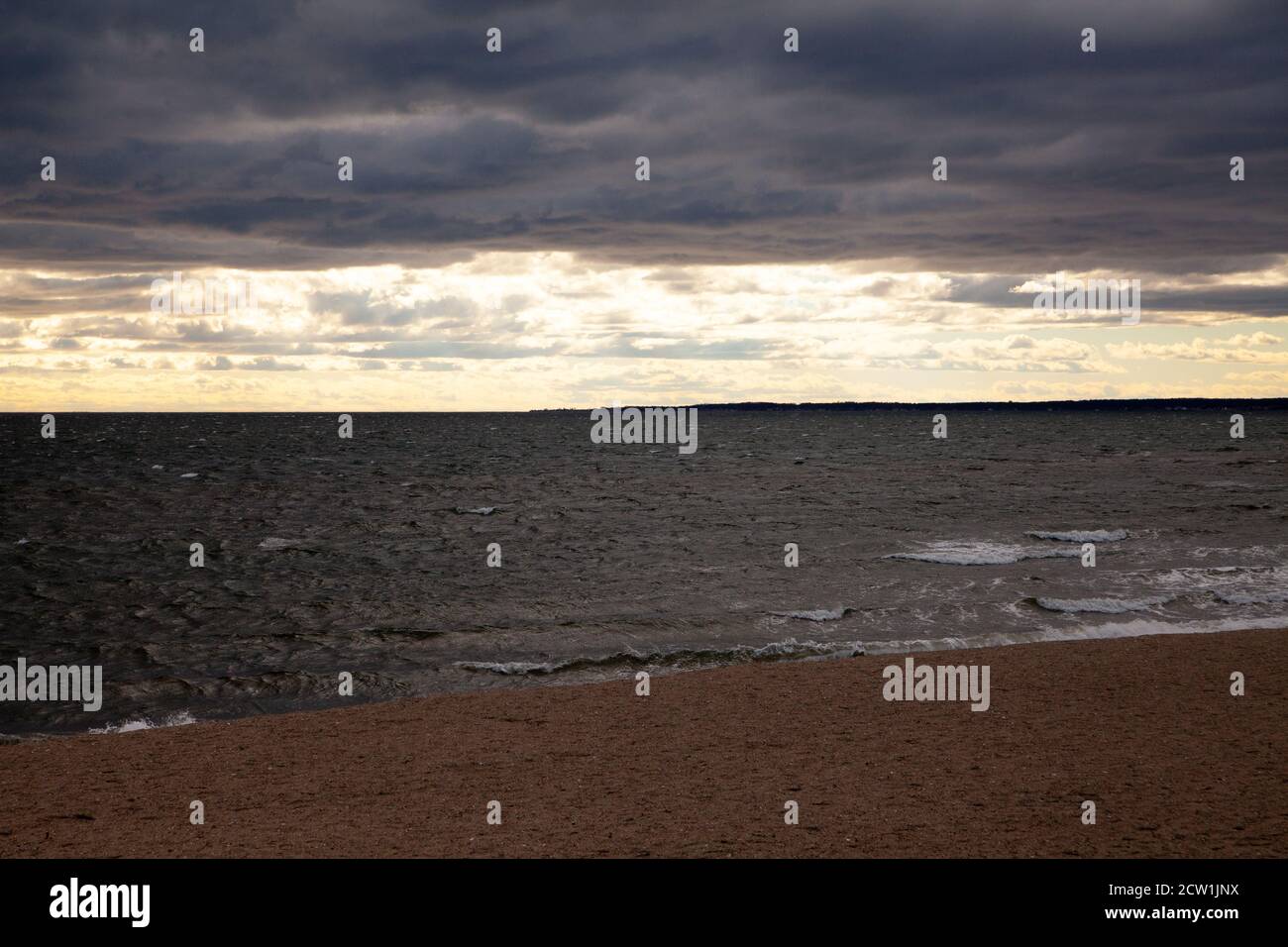 Der Sonnenuntergang über dem Meer - düstere Wolken über dem Strand und dunkles Wasser, und helle goldene Wolken über dem Horizont. Stockfoto