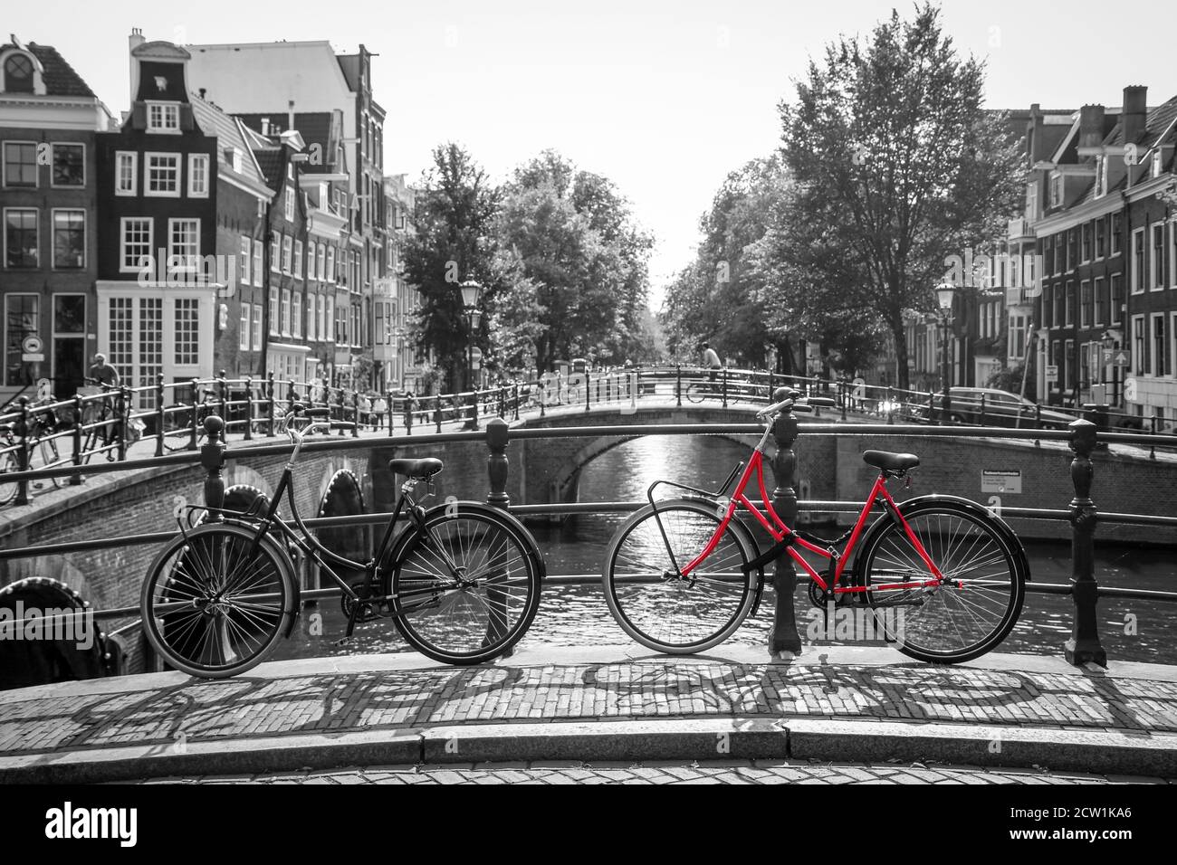 Ein Bild von einem roten Fahrrad auf der Brücke über den Kanal in Amsterdam.  Der Hintergrund ist schwarz-weiß Stockfotografie - Alamy