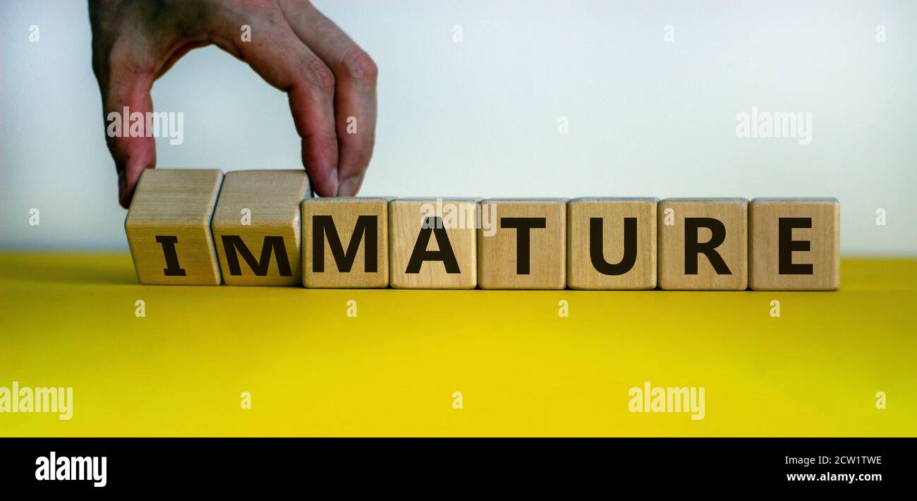 Hand dreht einen Würfel und ändert den Ausdruck "unreif" in "mature". Schöner gelber Tisch, weißer Hintergrund, Kopierraum. Geschäftskonzept. Stockfoto