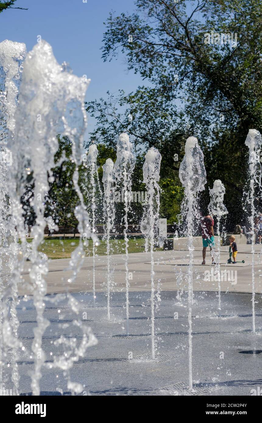Nikolaev, Ukraine - 17. August 2020: Die Bewohner flanieren neben den kühlen Bächen des Stadtbrunnens auf dem Stadtplatz. Jets von kühlem klarem Wasser Gushi Stockfoto