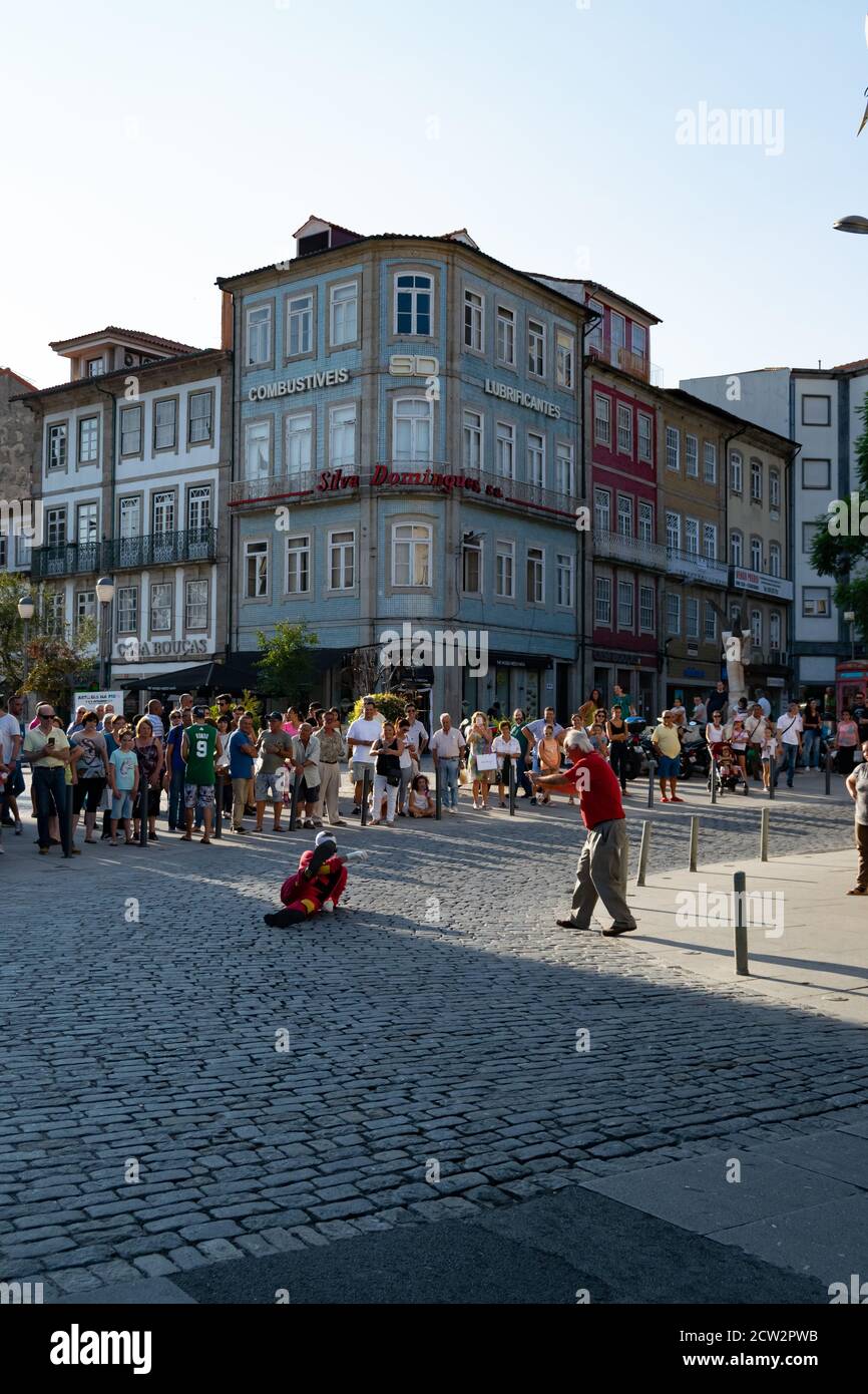 Älterer Mann, der mit Smartphone zu einem Clown fotografiert Auf dem Boden, während eine Gruppe von Personen beobachten In der portugiesischen Stadt Braga Stockfoto