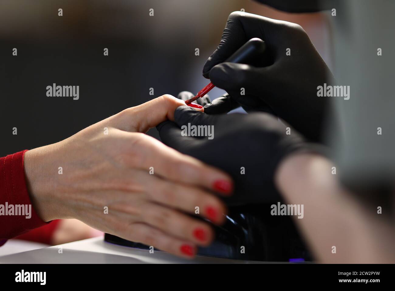 Handschuhen Maniküre Meister malt Nägel mit Pinsel in rot. Stockfoto