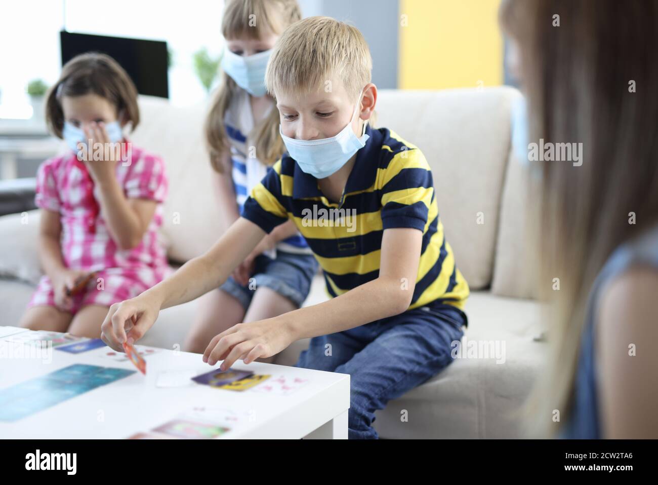 Kinder in medizinischen Schutzmasken spielen Brettspiele zu Hause. Stockfoto