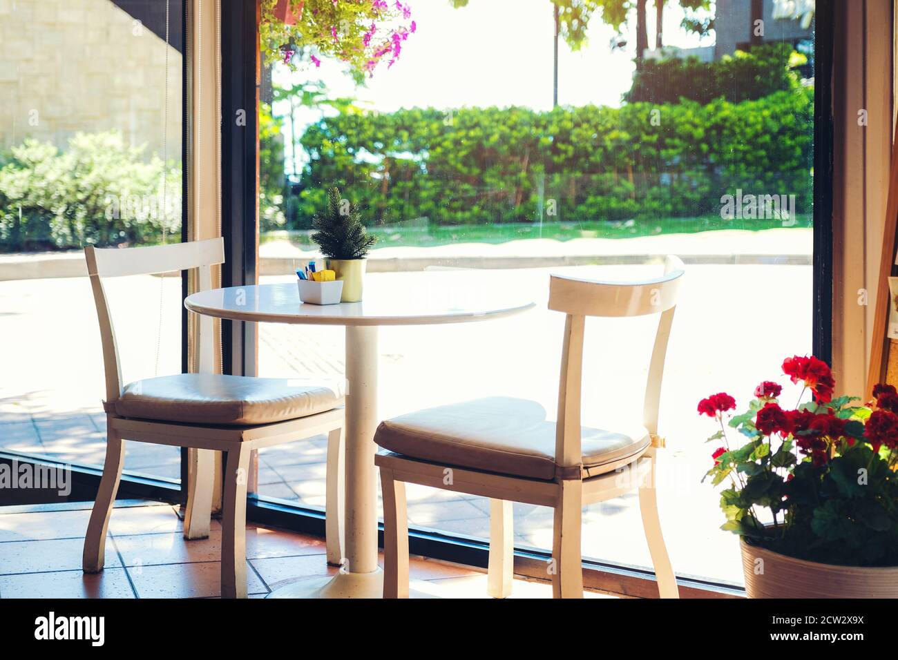 Ein Tisch in einem Café mit Blumentopf. Zwei leere Stühle warten auf  Kunden, innen mit landschaftlich schönem Blick auf das Meer aus dem  Glasfenster Stockfotografie - Alamy