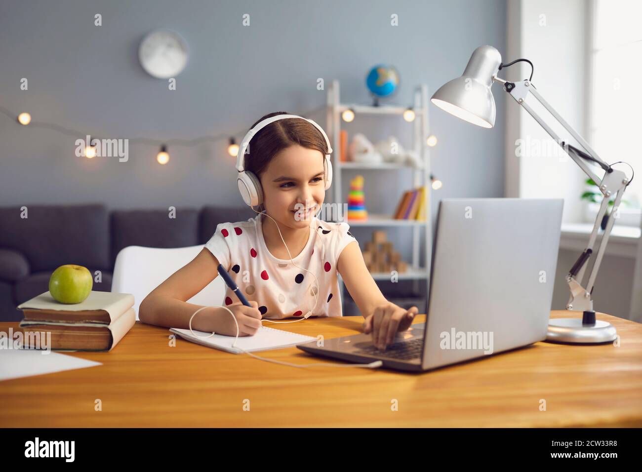 Online-Schulbildung zu Hause. Fleißiges kleines Mädchen im Headset beobachten Online-Unterricht auf Laptop Stockfoto