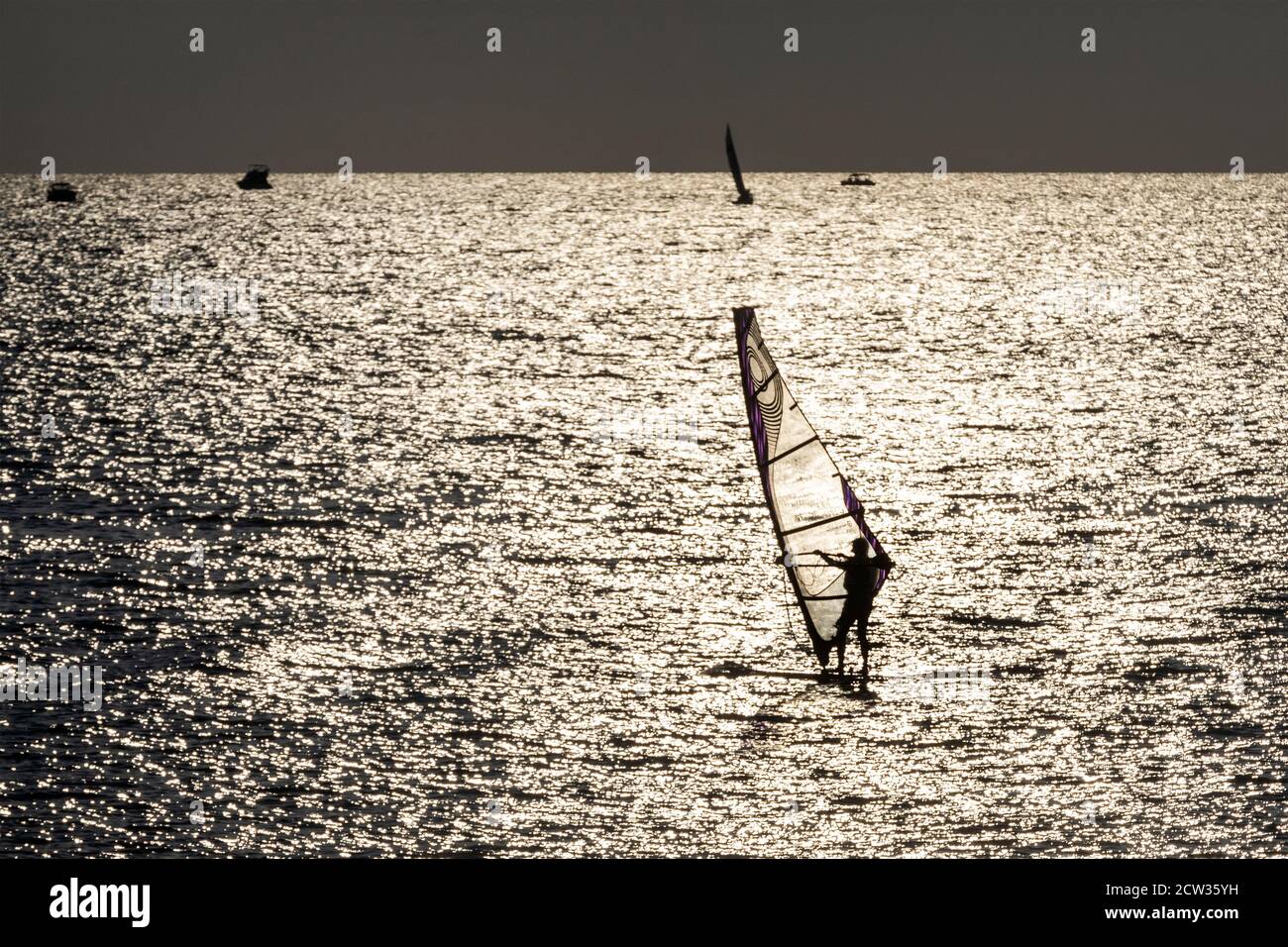 Eine Silhouette eines Windsurfers vor einem Sonnenuntergang Hintergrund auf Eine Meeresoberfläche, die Wind und Welle fängt Stockfoto