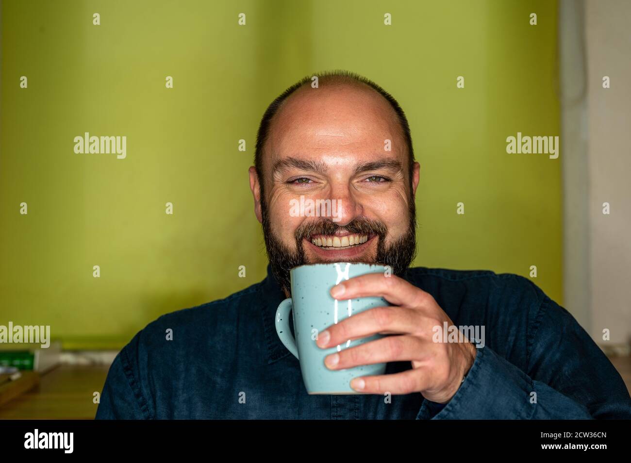 Mann mit Kaffeetasse in der Hand lacht freundlich an der Kamera Stockfoto