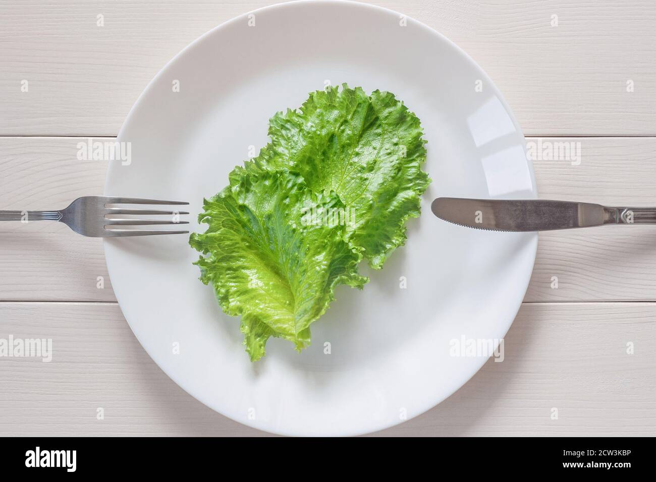 Monotrophe Ernährung - zwei Blätter Salat auf dem Teller, Gabel und Messer, Holzhintergrund Stockfoto
