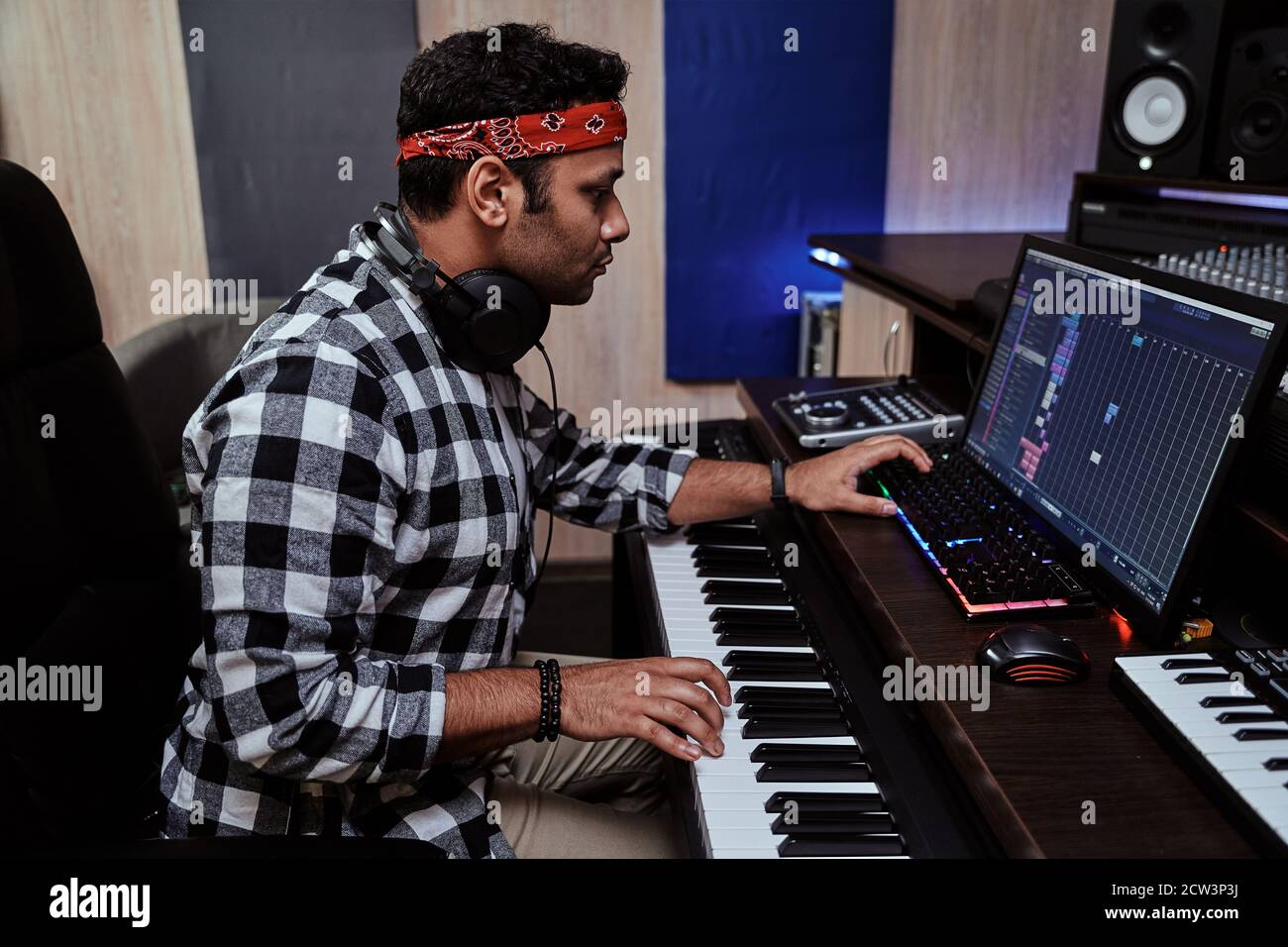Junger Mann, männlicher Künstler, der konzentriert auf Keyboard-Synthesizer spielt und im Aufnahmestudio sitzt Stockfoto