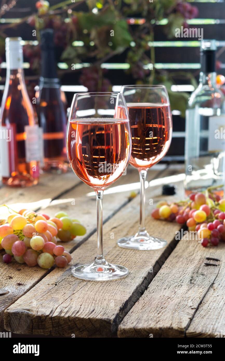 Volle Gläser Roséwein, Erholung im Freien, Holztisch mit Gläsern Wein,  Flaschen Wein und Trauben Stockfotografie - Alamy