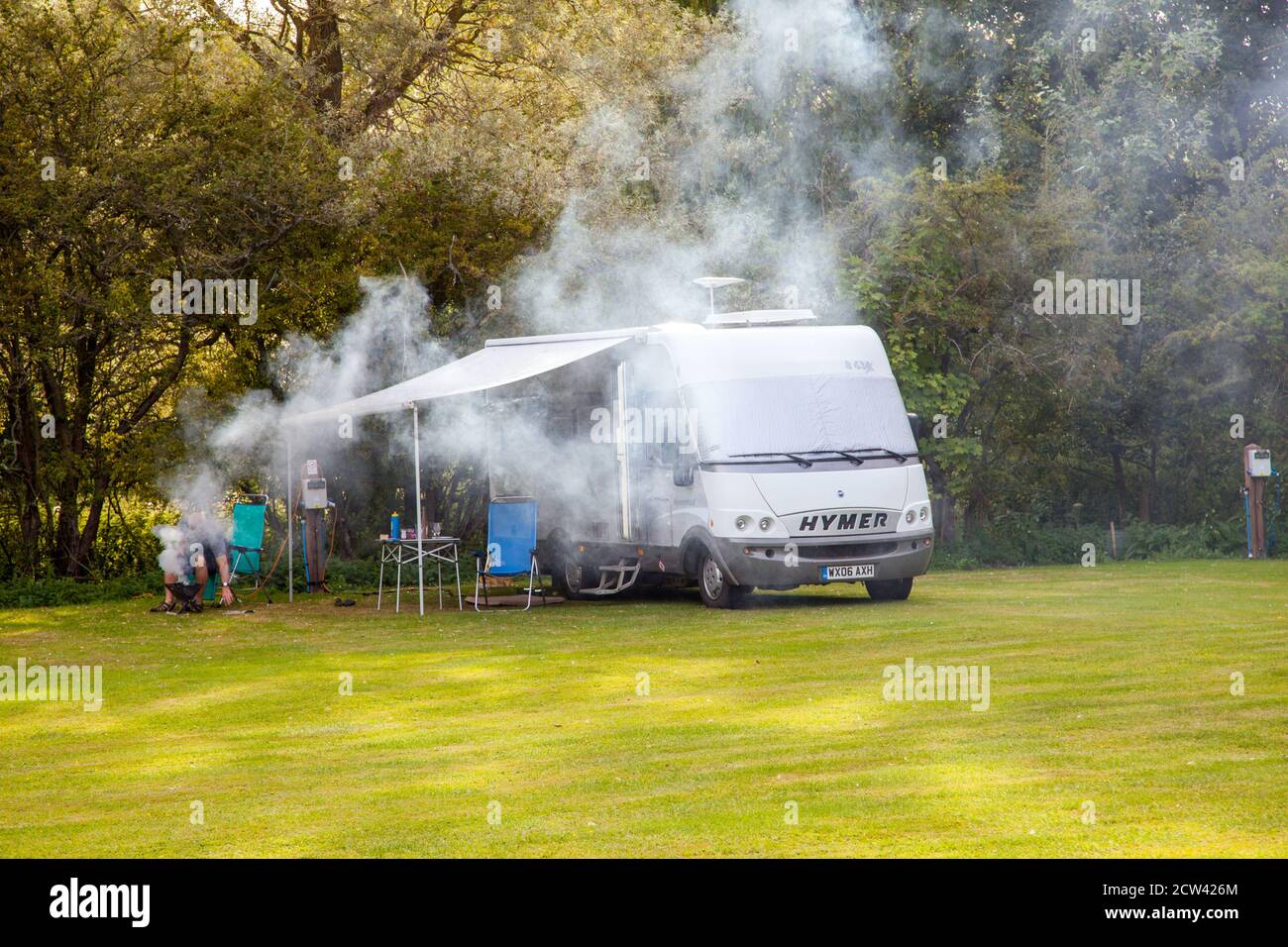 Mann macht viel Rauch Grillen vor seinem Wohnmobil Wohnmobil auf einem kleinen Campingplatz Stockfoto