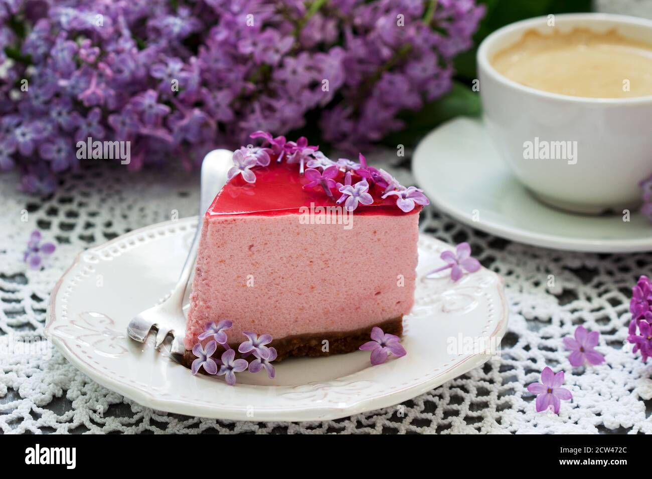 Ein mit lila Blüten dekorierter Beerenmousse mit Schokoladenbasis und Saftgelee, serviert mit Kaffee. Stockfoto