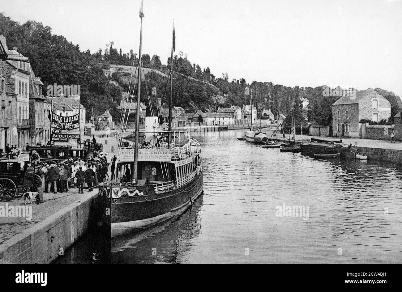 Ein historischer Blick auf die Kais von der alten Brücke in Dinan mit einem Boot zusammen mit Werbefahrten zum Hotel De L'Univers in Saint Malo flussabwärts aufgenommen. In Denin, Côtes-d'Armor, Bretagne, Frankreich, aus einer Postkarte um 1900. Stockfoto