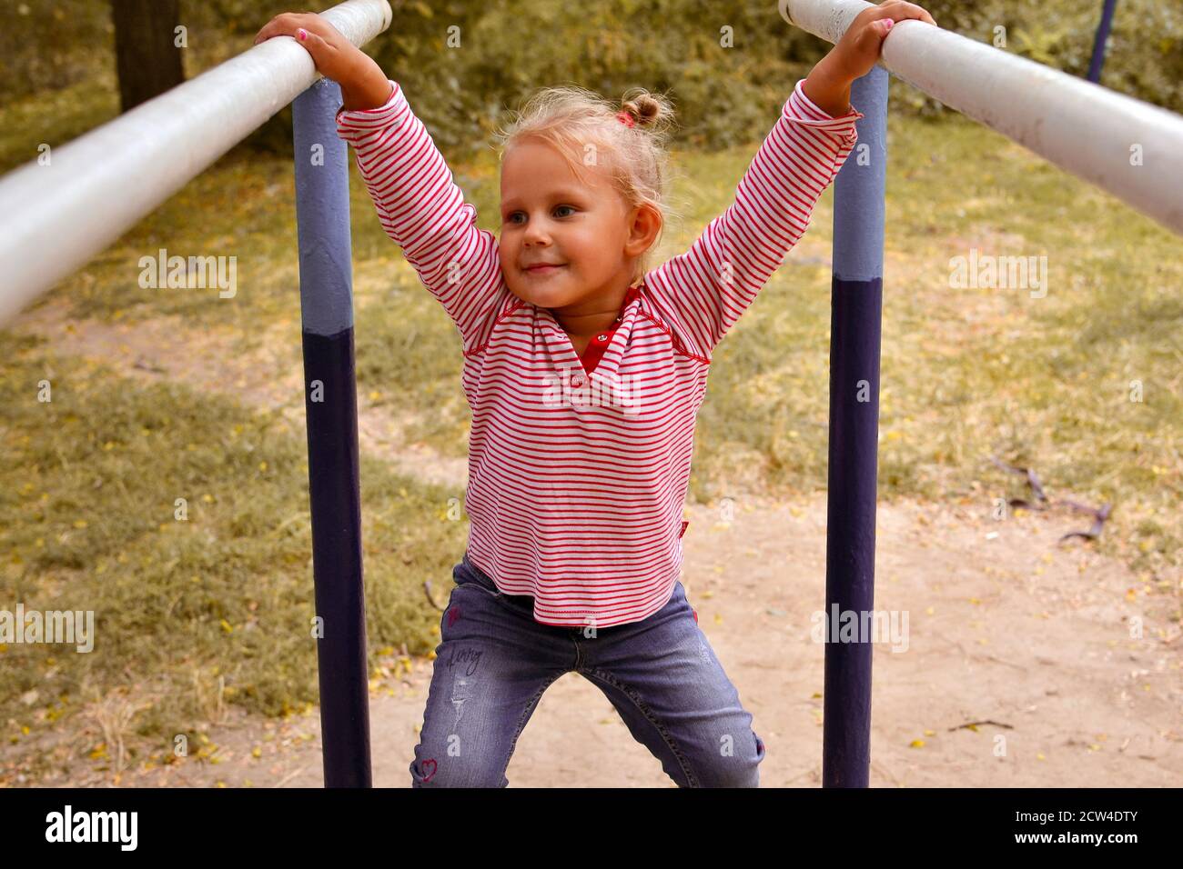 Ein süßes kleines Mädchen spielt an einem Herbsttag auf dem Spielplatz. Baby hängt an parallelen Stäben Stockfoto