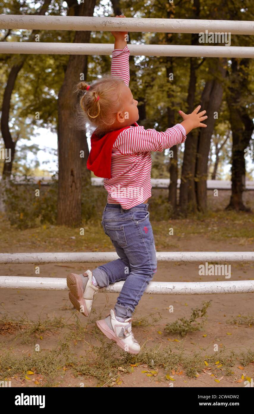 Ein süßes kleines Mädchen spielt an einem Herbsttag auf dem Spielplatz. Baby hängt an parallelen Stäben Stockfoto