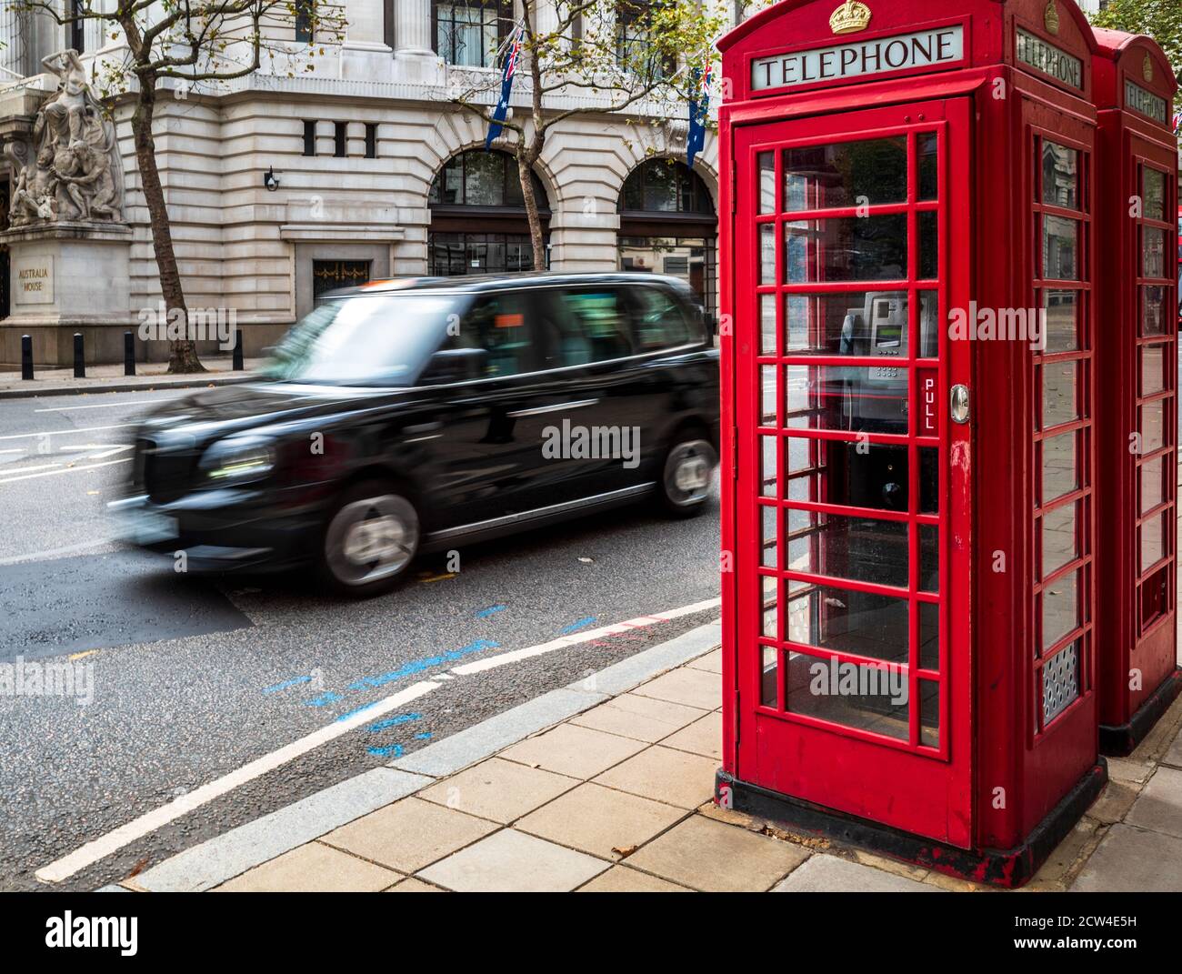 Ikonisches London - ein London Taxi fährt an zwei traditionellen roten Telefonzellen im Zentrum von London vorbei. Bewegungsunschärfe der Taxibewegung. London Tourism. Stockfoto