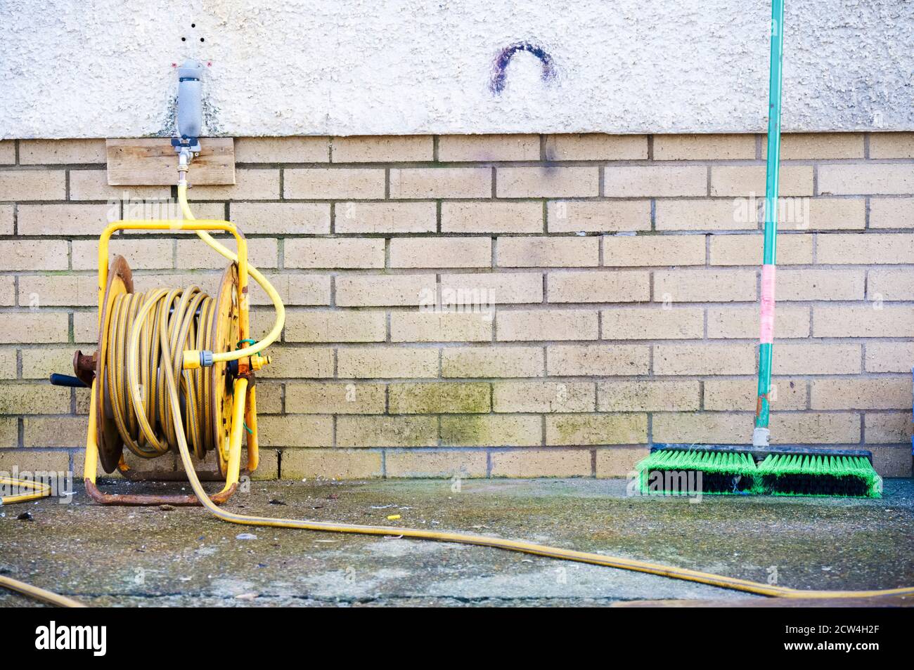 Gelber Gummischlauch und grüne Bürste im Freien Stockfoto