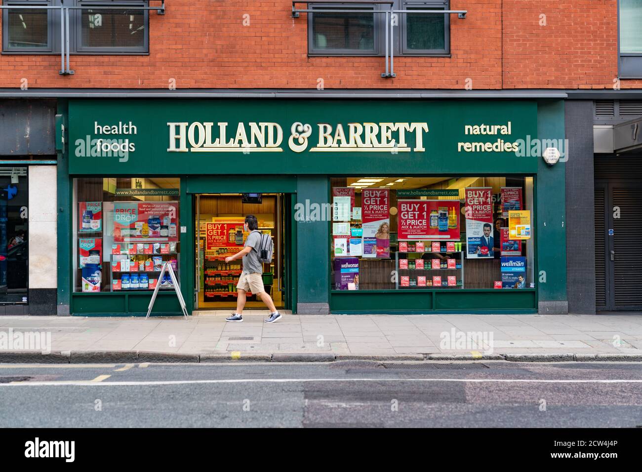 LONDON, ENGLAND - 24. JULI 2020: Holland & Barrett Health Food Store in Holborn, London während der COVID-19 Pandemie mit einem Mann, der vorne in der Kleidung läuft Stockfoto