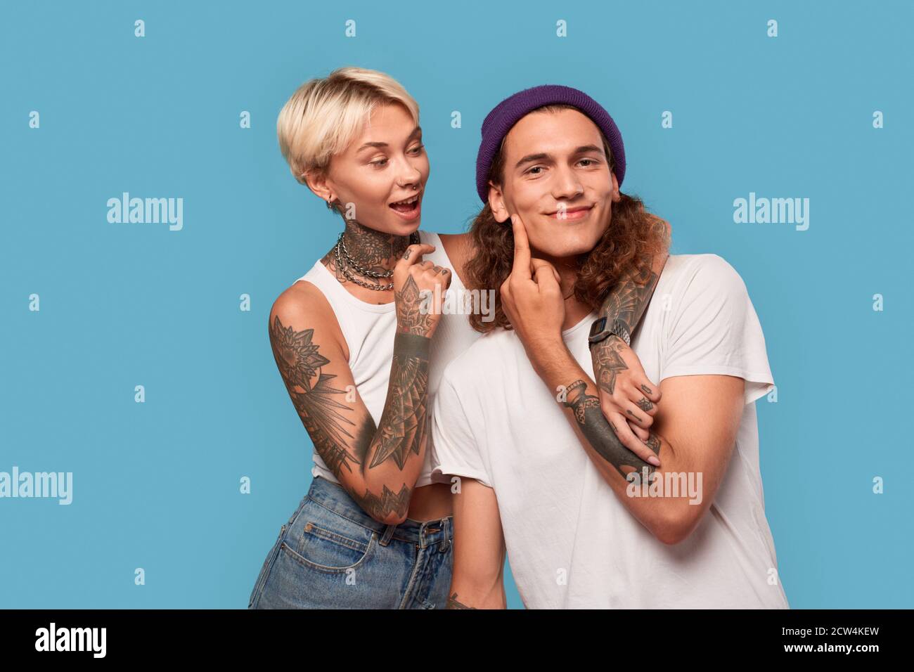 Freistil. Junge tätowierte Paar isoliert auf blau Freundin umarmt Freund fragen, ihn freudig küssen Stockfoto