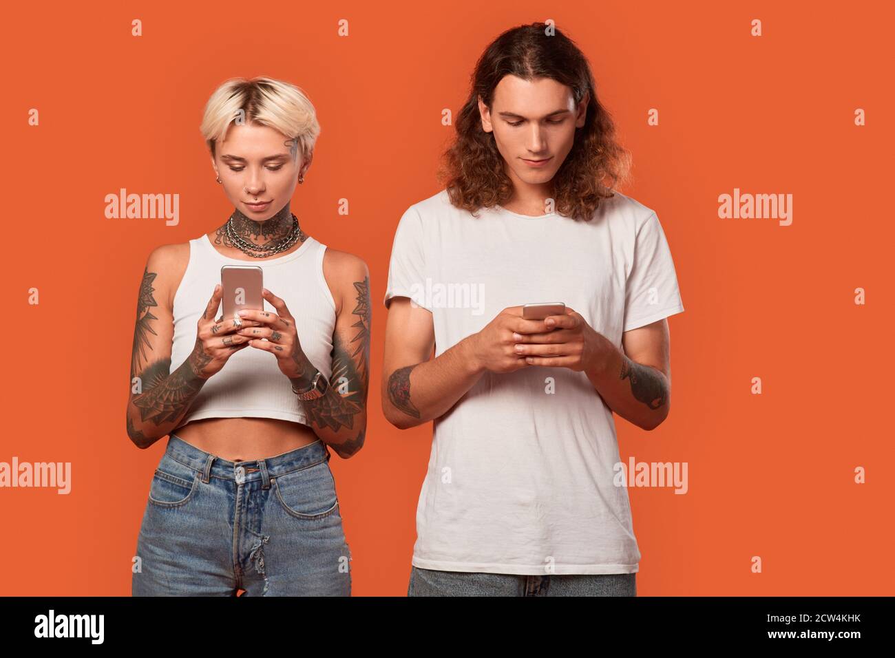 Freistil. Junge tätowierte Paar stehend isoliert auf orange browsing Smartphone konzentriert antisozial Stockfoto