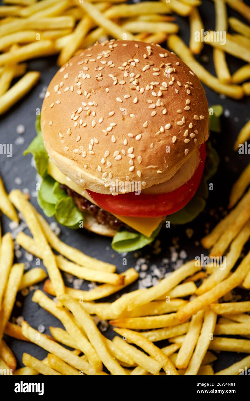 Cheeseburger umgeben von pommes auf einem schwarzen Tisch Stockfoto