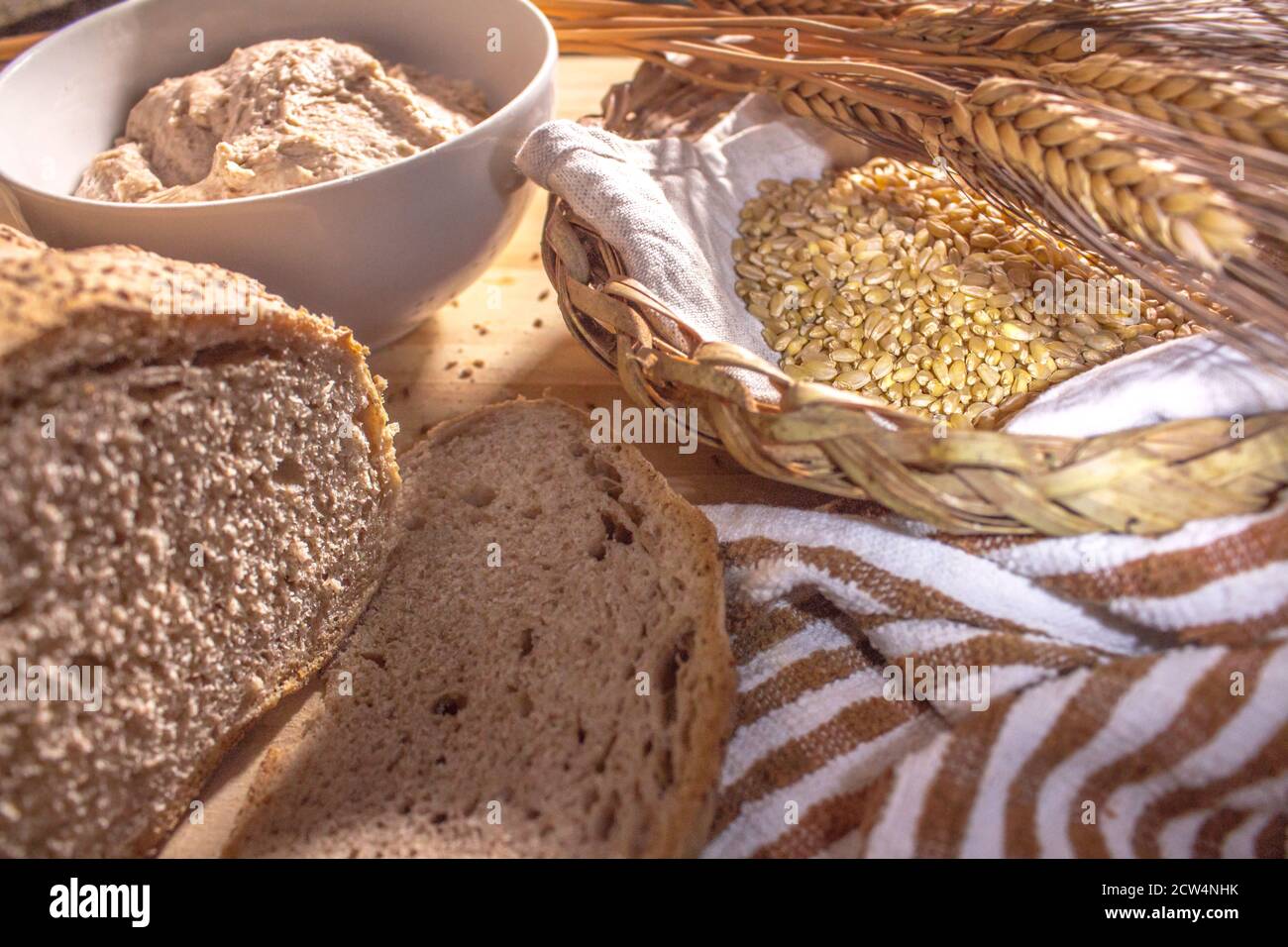 Weidenkorb mit Weizen und etwas Weizenohren, hausgemachtem Vollkornbrot und einer Tasse Sauerteig Stockfoto