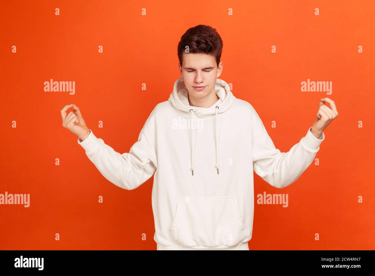 Schöner Teenager im lässigen Stil Sweatshirt hält die Hände in Mudra Geste schließen Augen, Yoga üben, Rituale für Glück vor Prüfungen. Innenst Stockfoto