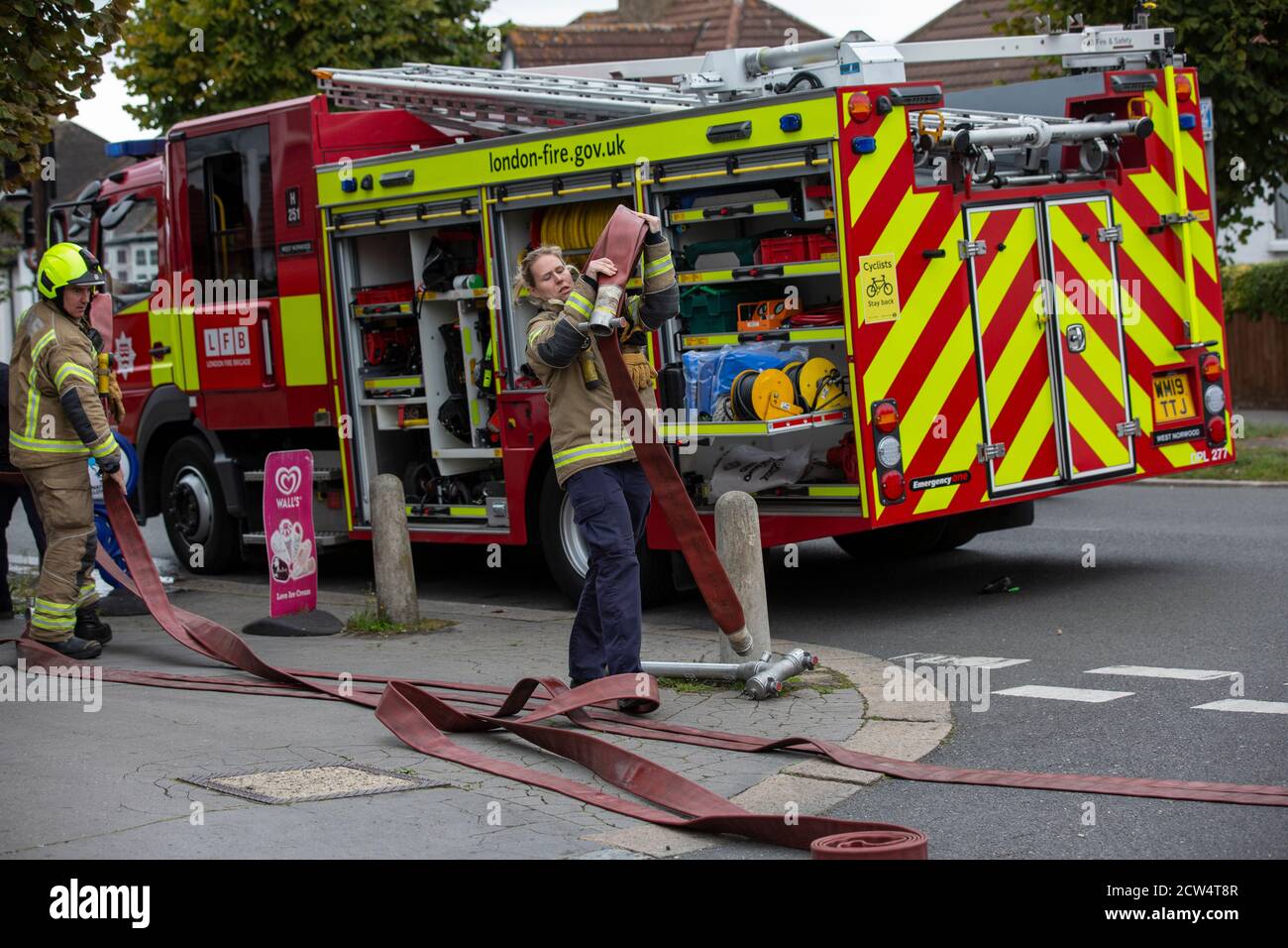 Die Feuerwehrfrau rollt den Schlauch mit der Londoner Feuerwehr aus, die an einem Hausbrand in einer Wohnstraße in South London, England, Großbritannien teilnimmt Stockfoto