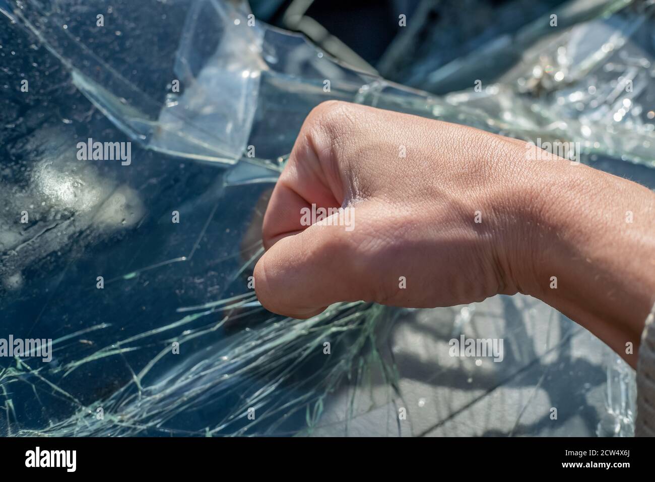 Die Faust eines Mannes gegen die zerbrochene Windschutzscheibe. Risse an der Windschutzscheibe des Fahrzeugs durch den Aufprall Stockfoto