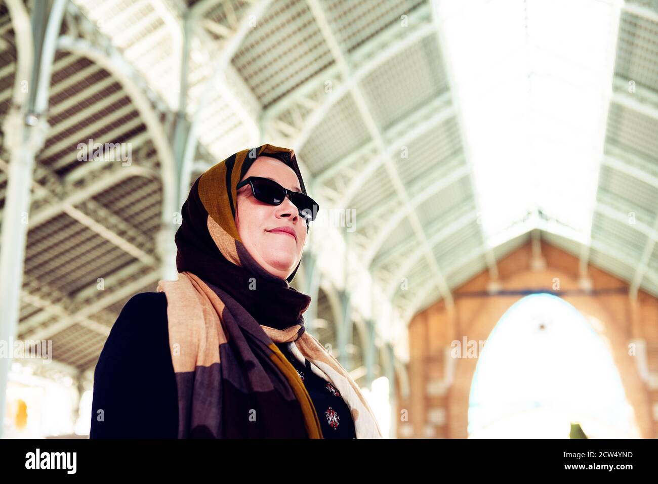 Muslimische Frau in Kopftuch und Sonnenbrille in einem Gelände mit einem Metalldach. Copy Space Stockfoto