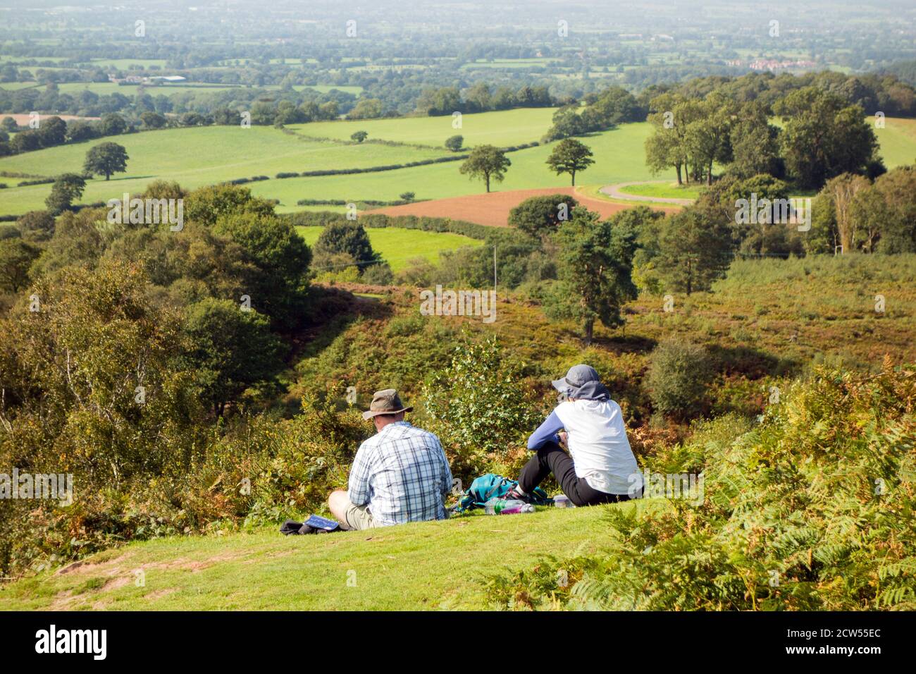 Mann und Frau ruhen sich aus, während sie auf dem Sandstone Trail auf Bickerton Hills Cheshire wandern, mit Blick über die Cheshire-Ebene Stockfoto