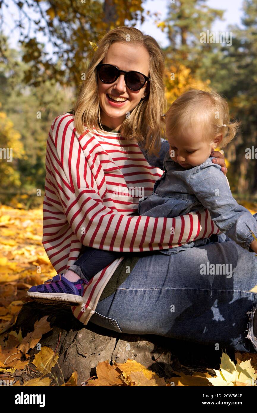 Herbstspaziergang mit der Familie im Wald. Schöner Park mit trockenen gelben und roten Blättern. Liebevolle Mutter umarmt Tochter Stockfoto