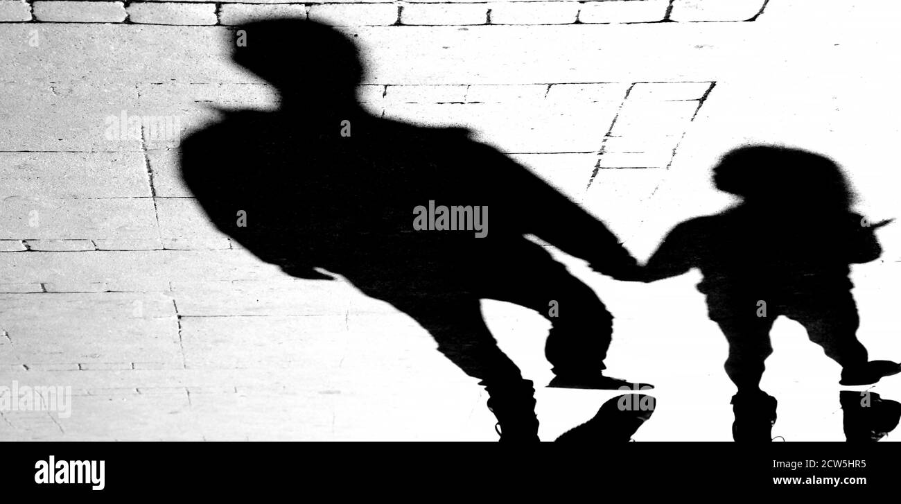 Silhouette Schatten eines Vaters Mann hält Hände mit Tochter Mädchen auf Stadt Bürgersteig in hohem Kontrast schwarz und weiß Stockfoto