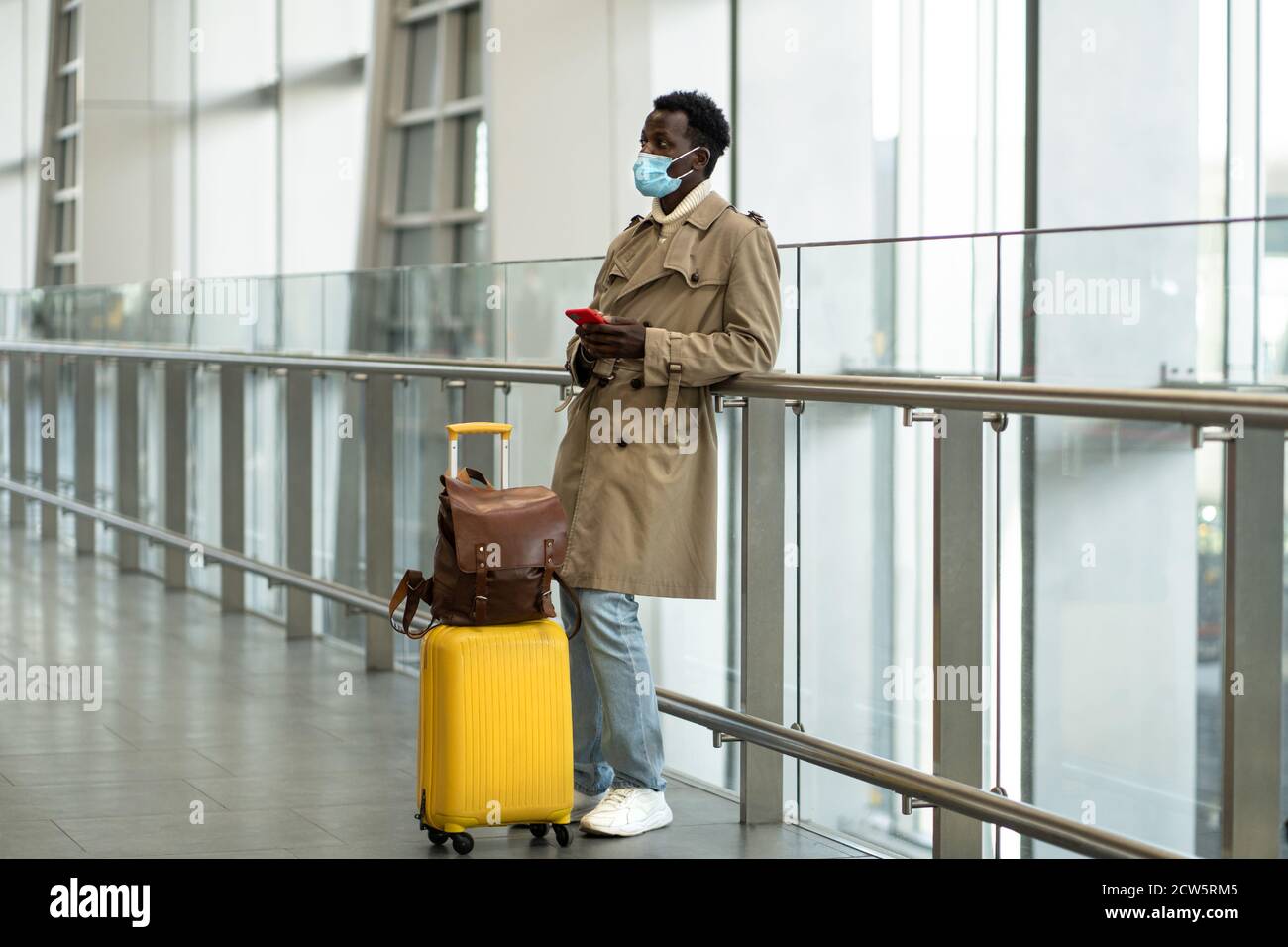 Afro-amerikanischer Reisender Mann mit gelben Koffer steht im Flughafen-Terminal, tragen Sie eine schützende Gesichtsmaske, um sich vor Grippe-Virus, Pandemie Cov zu schützen Stockfoto