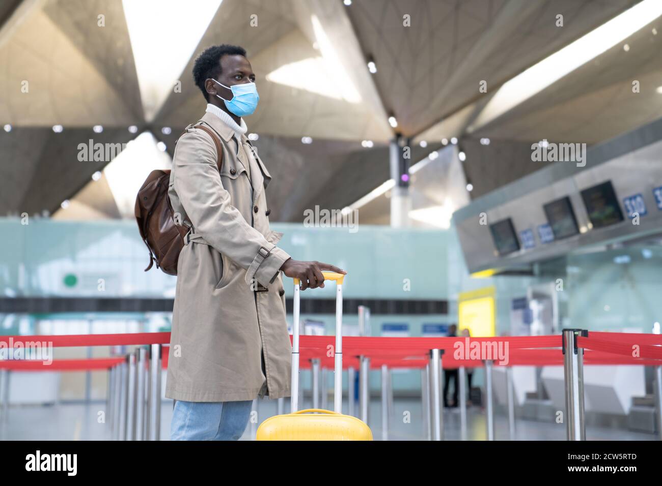Porträt eines schwarzen Mannes mit Koffer trägt Gesichtsschutzmaske während Virus-Epidemie, covid-19 Pandemie, während am Flughafen-Terminal stehen. Stockfoto