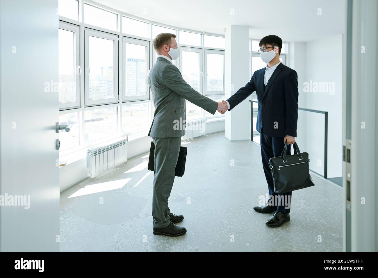 Zwei junge interkulturelle erfolgreiche Geschäftsleute, die sich im Korridor die Hände schüttelten Stockfoto