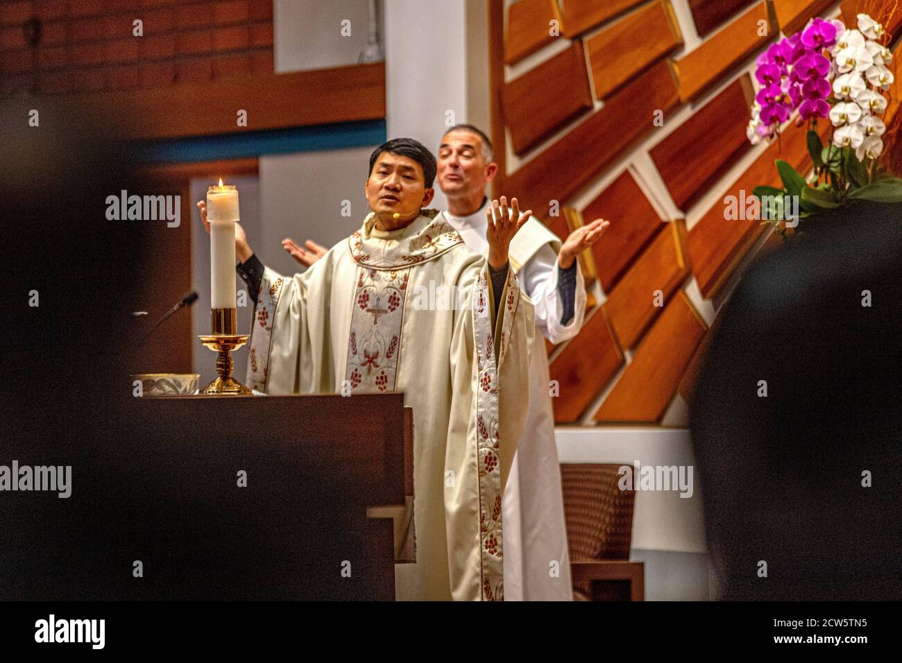 In zeremoniellen Roben unterstützt ein Diakon einen asiatisch-amerikanischen Priester bei der Durchführung einer Messe am Altar einer katholischen Kirche in Südkalifornien. Stockfoto