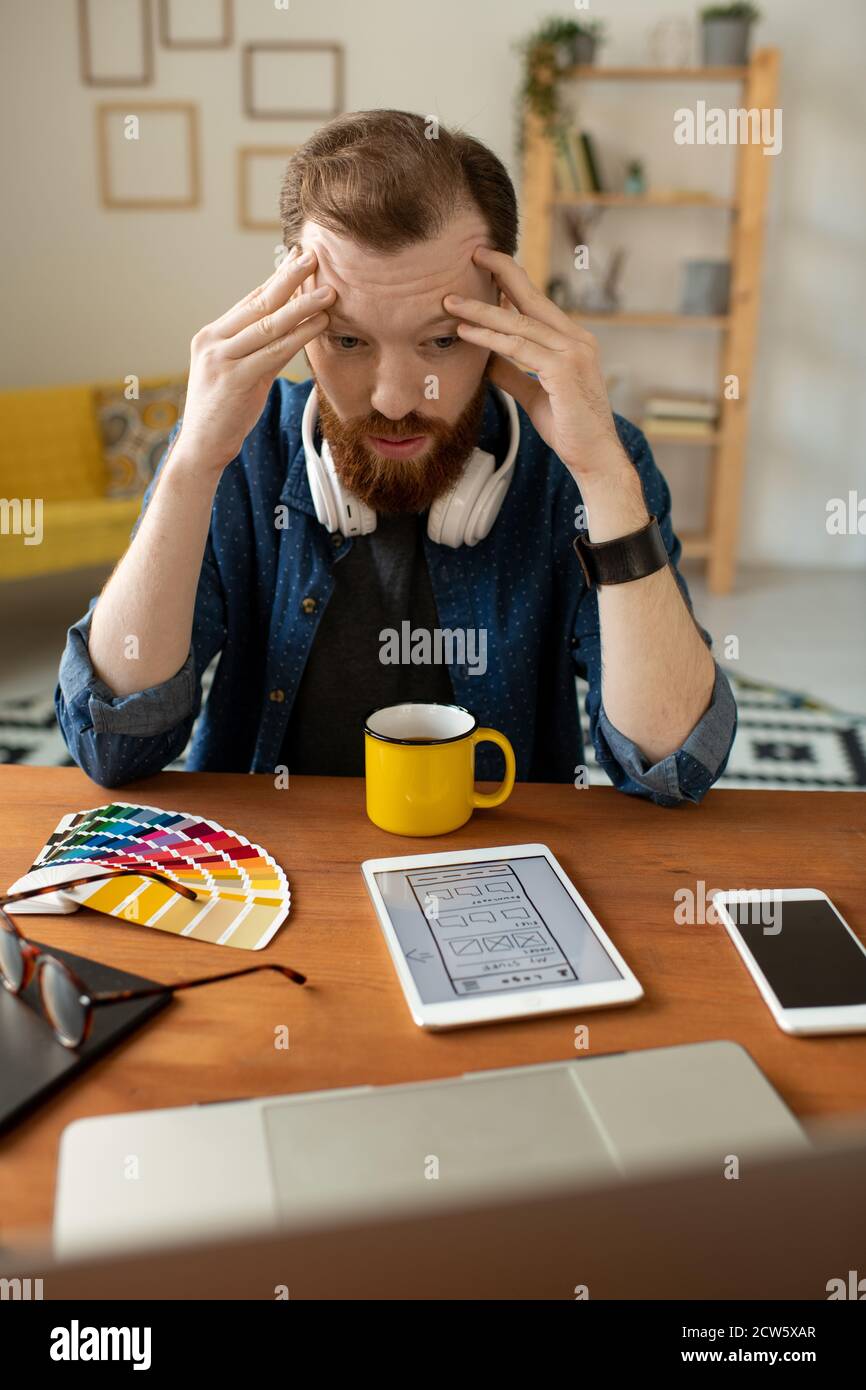 Junge müde Software-Entwickler berühren Stirn beim Biegen über Tisch Stockfoto