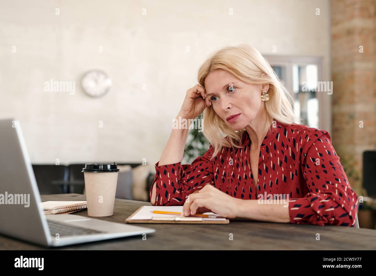 Serious reife blonde Geschäftsfrau Blick auf Online-Daten auf Laptop Anzeigen Stockfoto