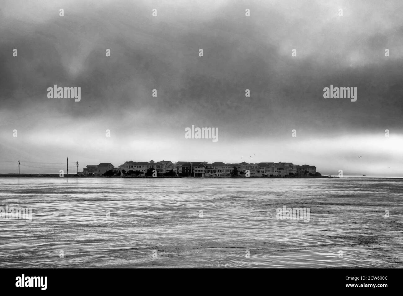 Schwarz-weißes Bild einer Gruppe von Inselgebäuden, umgeben von dunklen, brütenden Wolken und rauem Meer. Stockfoto