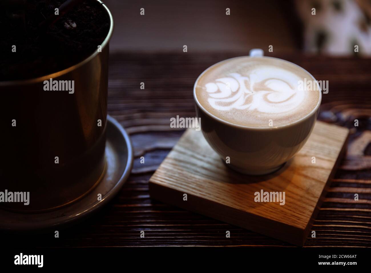 Latte Art Kaffeetasse auf Holztisch. Neben der Tasse befindet sich ein Blumentopf Stockfoto