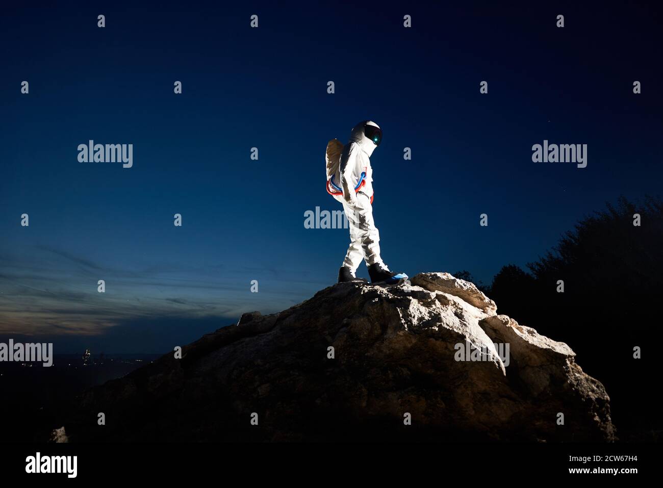 Volle Länge der Raumfahrer Erreichen der Spitze des felsigen Hügel mit schönen blauen Himmel auf Hintergrund. Astronaut trägt weißen Raumanzug mit Helm. Konzept der Weltraumforschung durch menschliche Rasse. Stockfoto