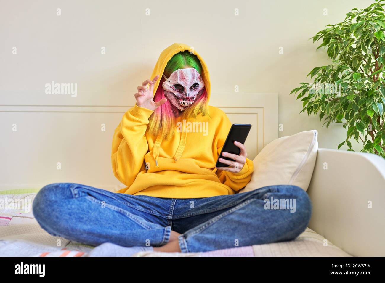 Halloween-Tag, Mädchen in gruseligen Gesichtsmaske mit Kapuze macht Videoanruf auf Smartphone Stockfoto