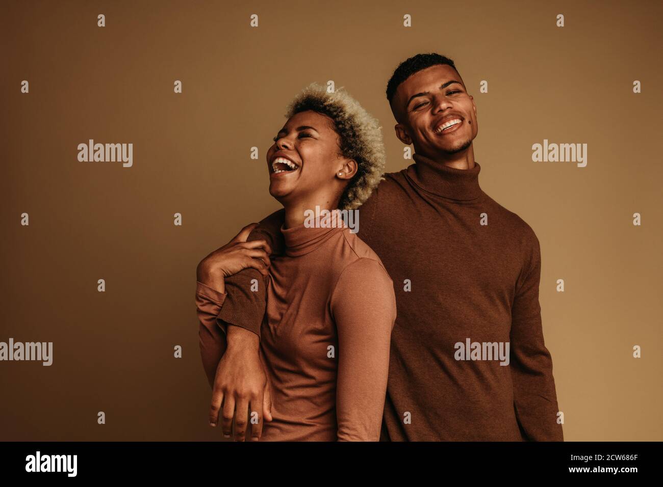 Liebespaar steht zusammen auf braunem Hintergrund. Glücklicher afroamerikanischer Mann und Frau, die lachen und einander halten. Stockfoto