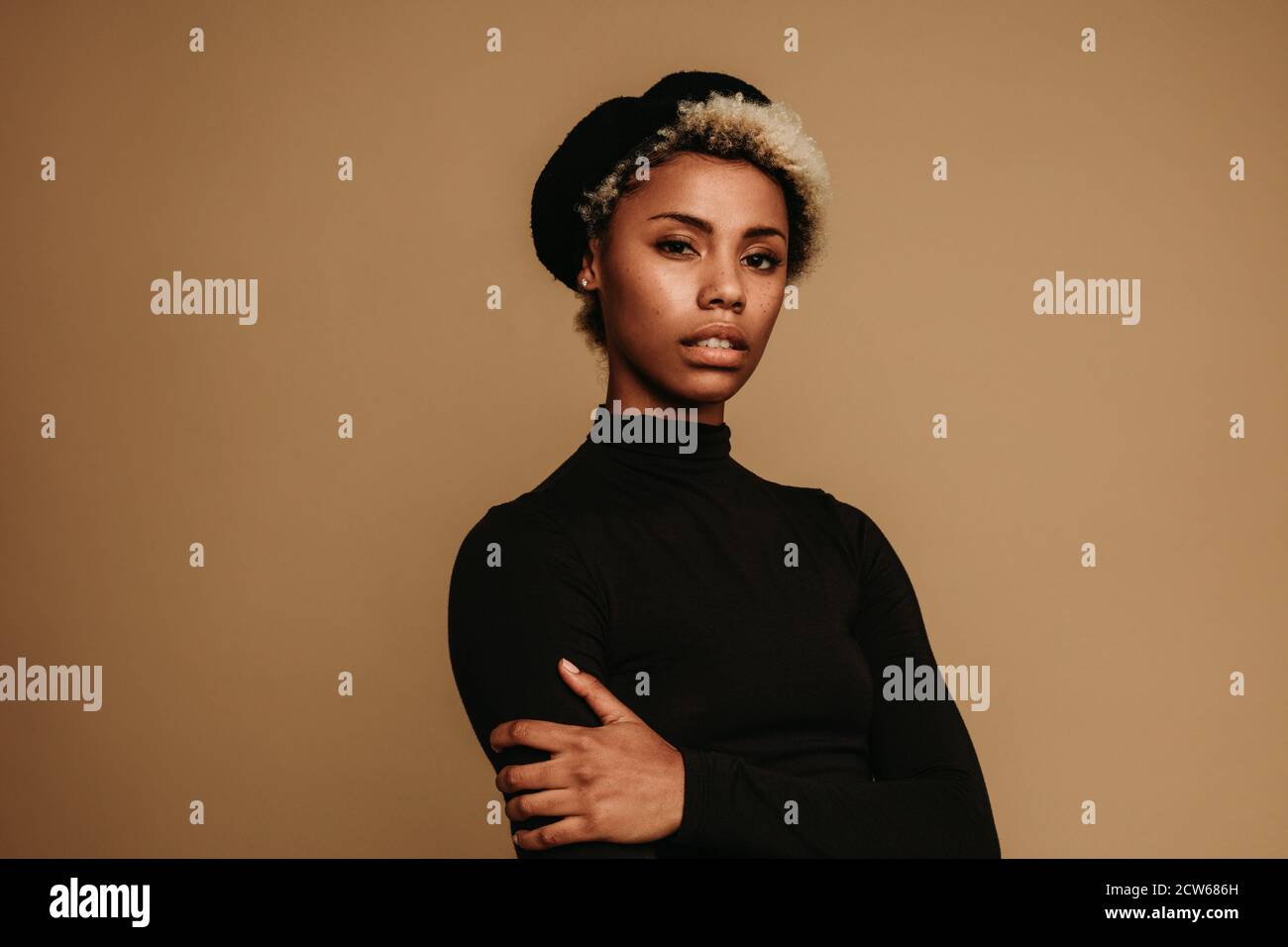 Porträt einer afroamerikanischen Frau in Mütze auf braunem Hintergrund. Fashion Frau steht mit gekreuzten Armen. Stockfoto