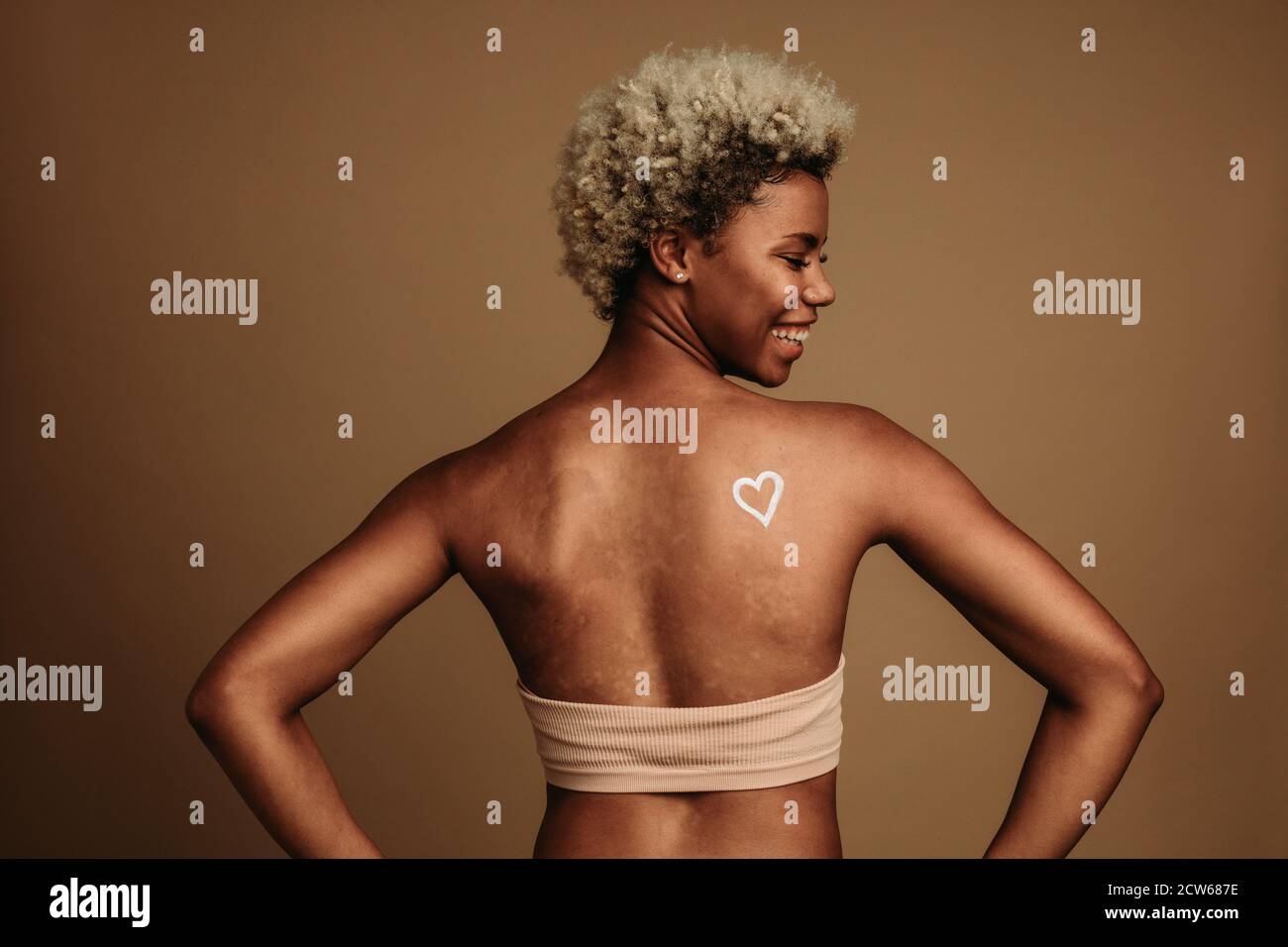 Black Lives Matter Aktivist steht auf braunem Hintergrund mit Herz auf der Rückseite gemalt. Porträt einer lächelnden afroamerikanischen Frau. Stockfoto