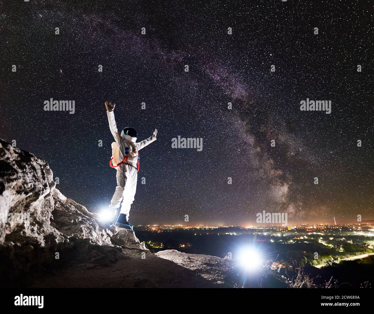 Astronaut hebt die Arme, während sie auf einem felsigen Berg mit fantastischem Sternenhimmel und Milchstraße im Hintergrund steht. Spaceman trägt weißen Raumanzug und Helm. Konzept der Raumfahrt Stockfoto