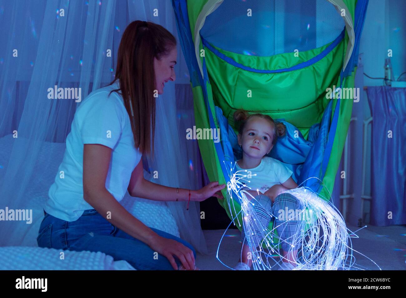 Kind und Therapeut im sensorisch anregenden Raum, snoezelen. Autistisches Kind, das während der Therapiesitzung mit farbigen Lichtern interagiert. Stockfoto