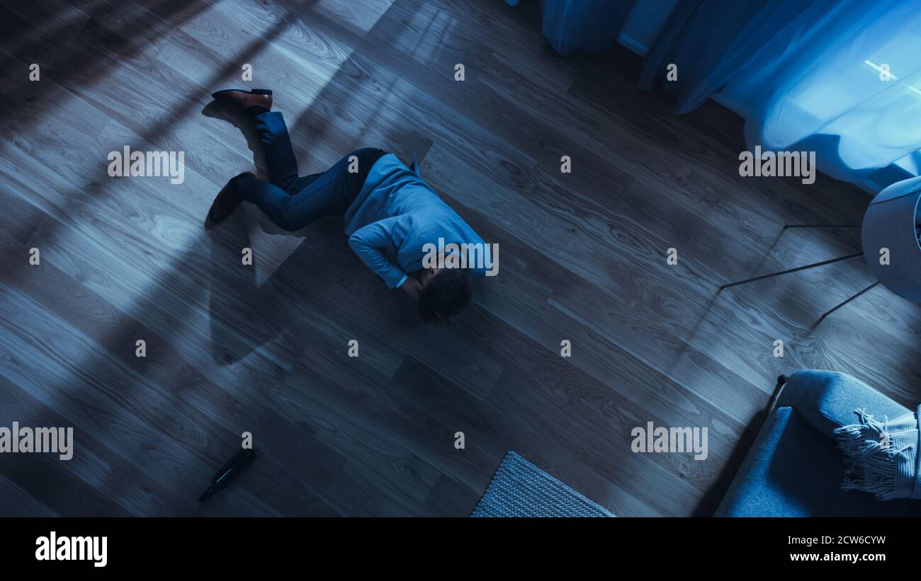 Armer depressiver betrunkener junger Mann kriecht in einer Wohnung mit Holzboden auf ein Sofa zu. Dramatische Kameraaufnahme Von Oben. Stockfoto