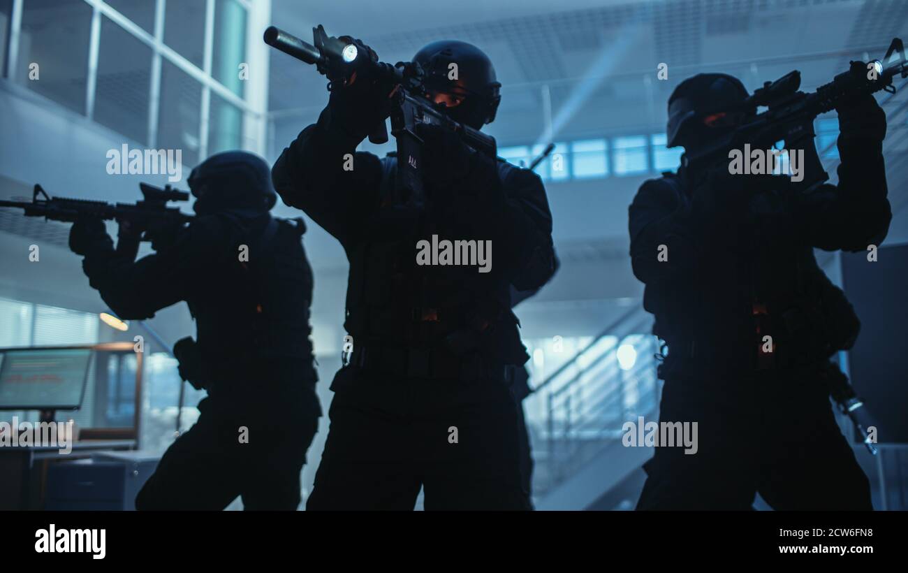 Maskierte Truppe bewaffneter SWAT-Polizisten steht im dunklen beschlagnahmten Bürogebäude mit Schreibtischen und Computern. Soldaten mit Gewehren und Taschenlampen surveil Stockfoto